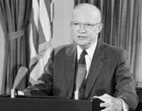 Black and white photograph of President Dwight D. Eisenhower delivering a speech from the Oval Office, with microphones in front and the U.S. flag in the background.